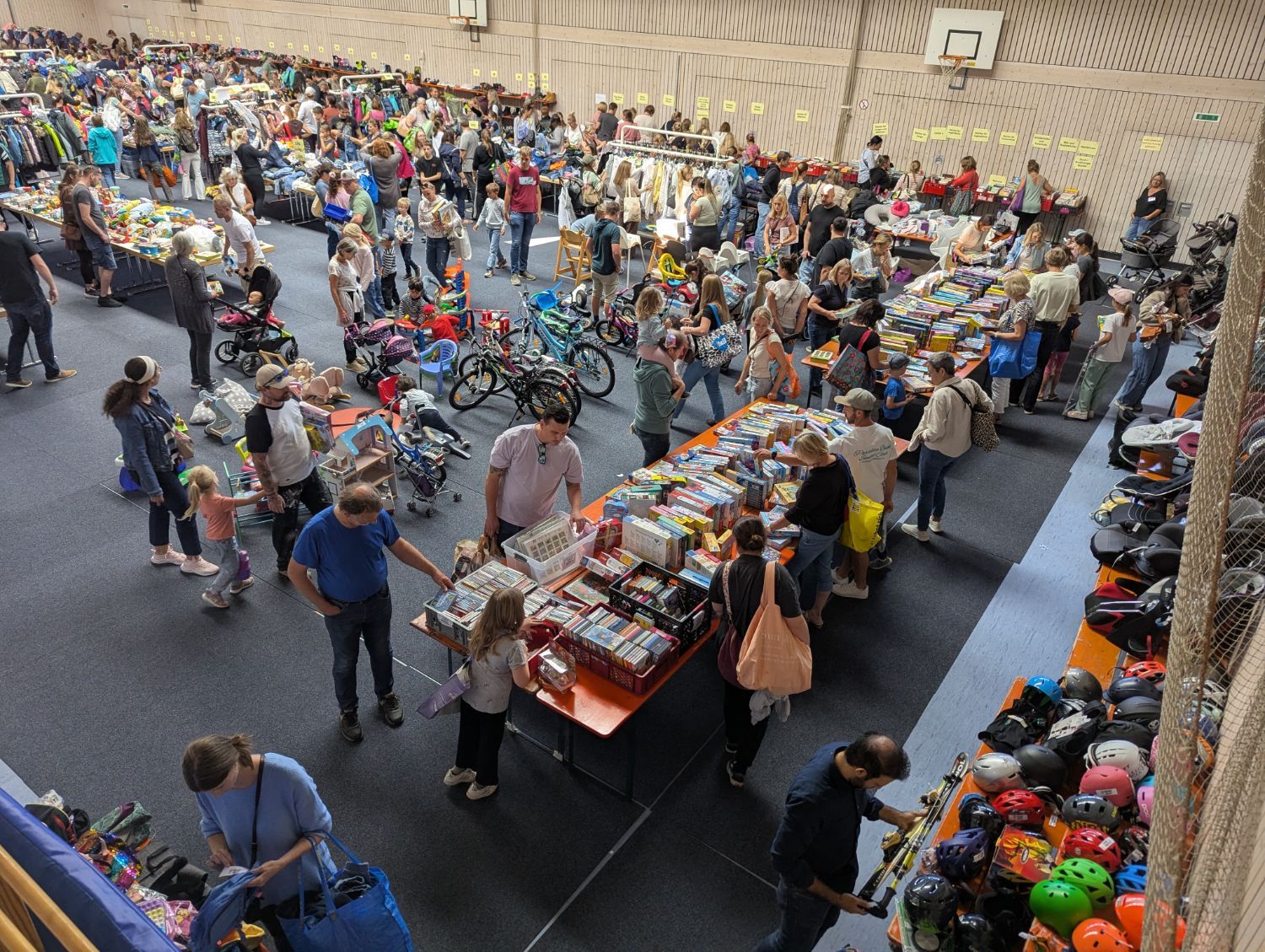 Tische mit Büchern, Spielen und CDs, dahinter Fahrräder und Kinderwagen, rechts Helme