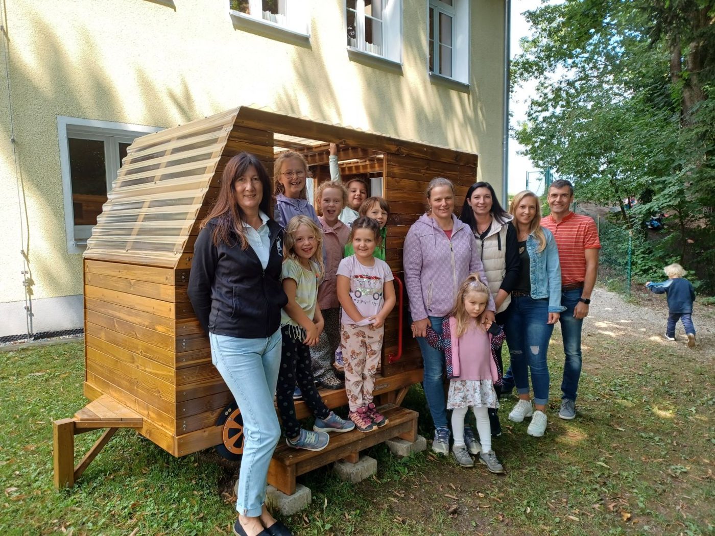 Kinder und Erwachsene vor dem neuen Holz-Wohnwagen im Kindergarten Armstorf